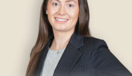 Professional headshot: Abby N. Ulman in pinstripe blazer against beige background.