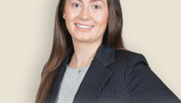 Professional headshot: Abby N. Ulman in pinstripe blazer against beige background.